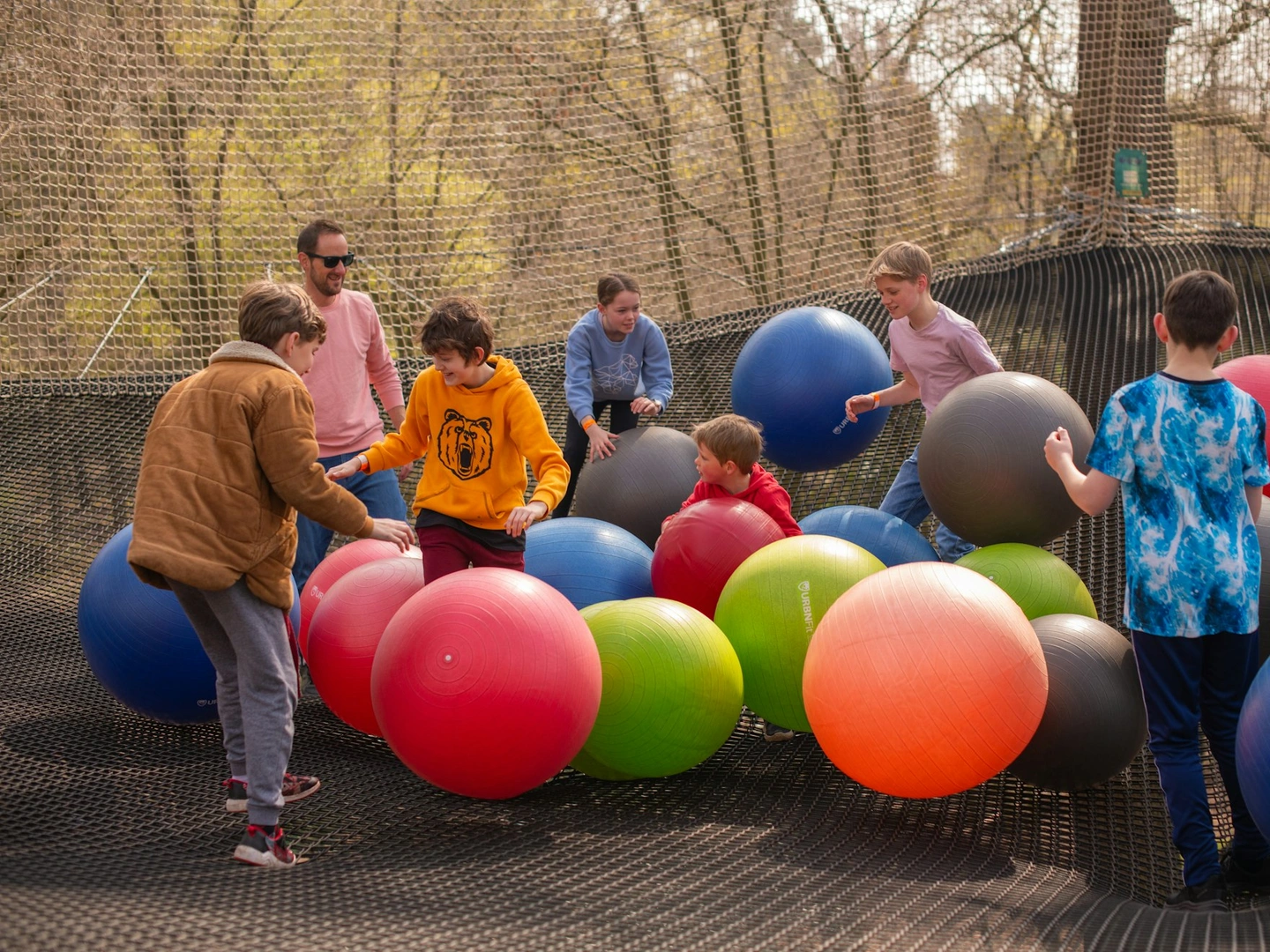 Group playing on a giant net suspended between trees with giant inflatable balls.