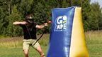 A man playing archery tag in field drawing his bow whilst hiding behind an inflatable barricade with Go Ape branding